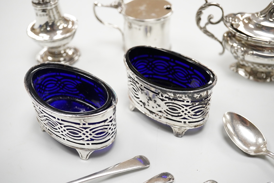 An ornate Edwardian silver oval mustard pot and matching spoon by Barker Brothers, Birmingham, 1902, length, 95mm, together with five other assorted silver condiments including a pair of pierced oval salts with blue glas
